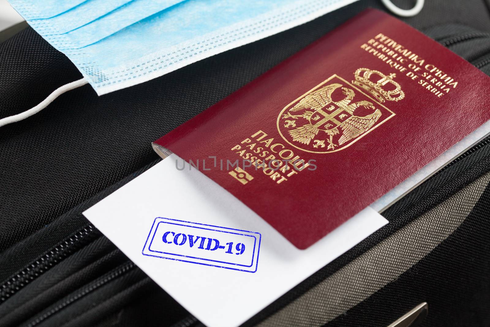 Passport and medical face mask on a suitcase, paper with COVID-19 stamped onto it, point of care testing at airport or border crossing facility,medical security health check to determine immunity