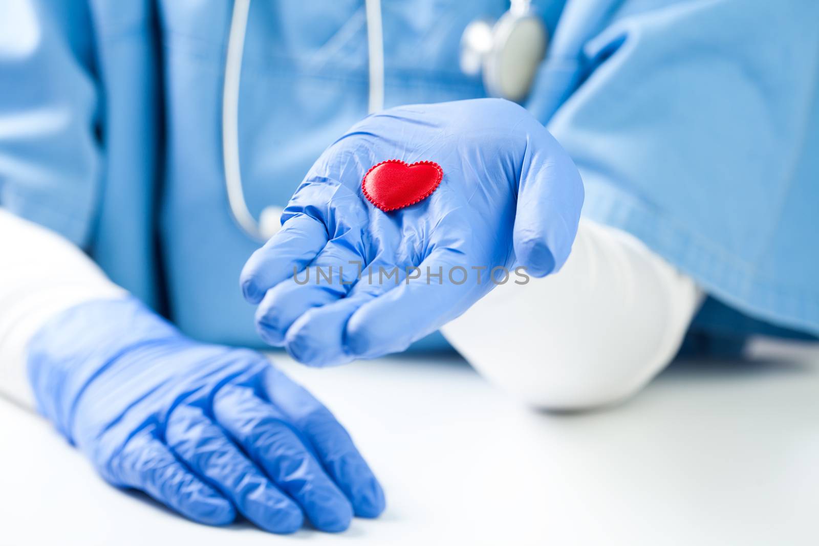 Female doctor holding small red heart on palm of hand, wearing blue NHS uniform, detail closeup, frequent healthcare check up and disease prevention concept, Coronavirus COVID-19 global crisis 