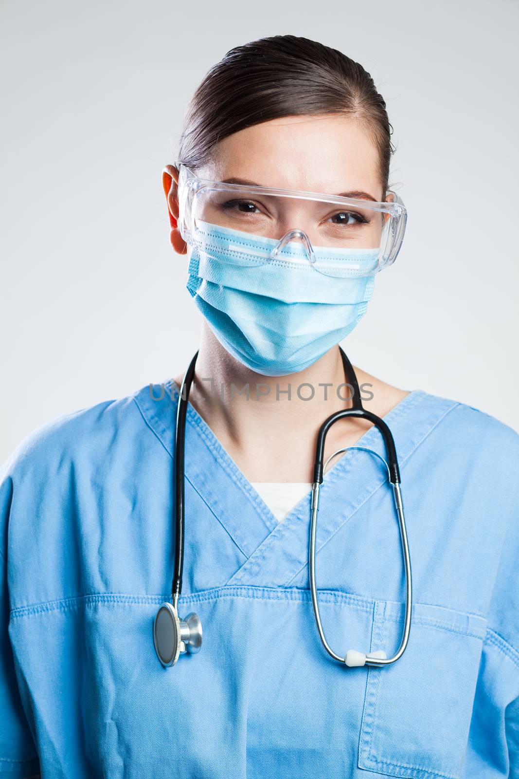 Happy satisfied female UK NHS doctor wearing protective face mask & safety goggles,eyes smiling,studio portrait isolated on white background,content relief after end of global COVID-19 pandemic crisis