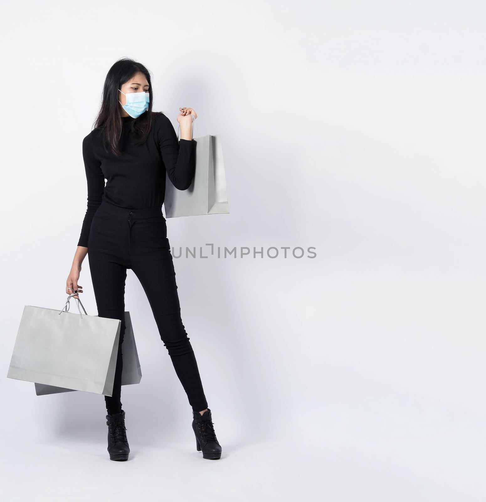 Asian woman holding shopping bags in her hand and wearing medical face mask to protect coronavirus or Covid 19 that is pandemic virus which represent shopper in new normal situatiuon and shop lover.
