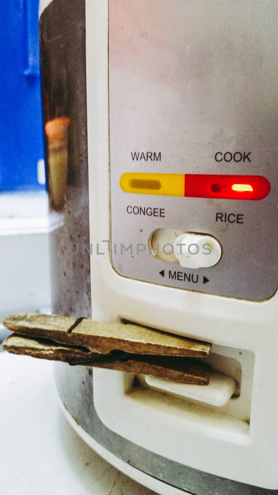 Damaged rice cooker, supported by a clothes hook so it can work, concept or humor image