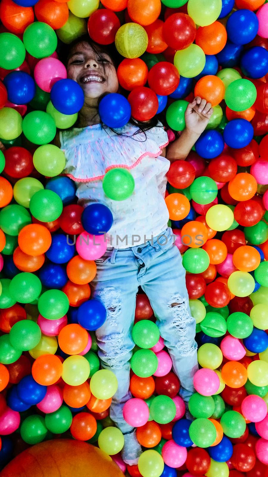 little smiling girl playing lying in colorful balls park playground