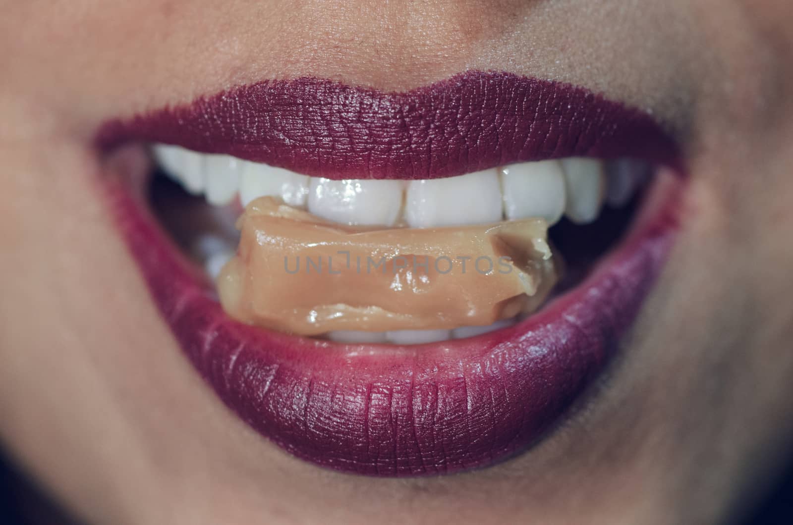 Close-up of woman mouth biting caramel candy with red lips