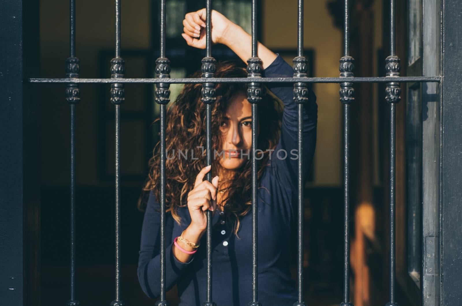 Young girl closed behind bars, network, as in prison. looking sexy with serious and smiling look