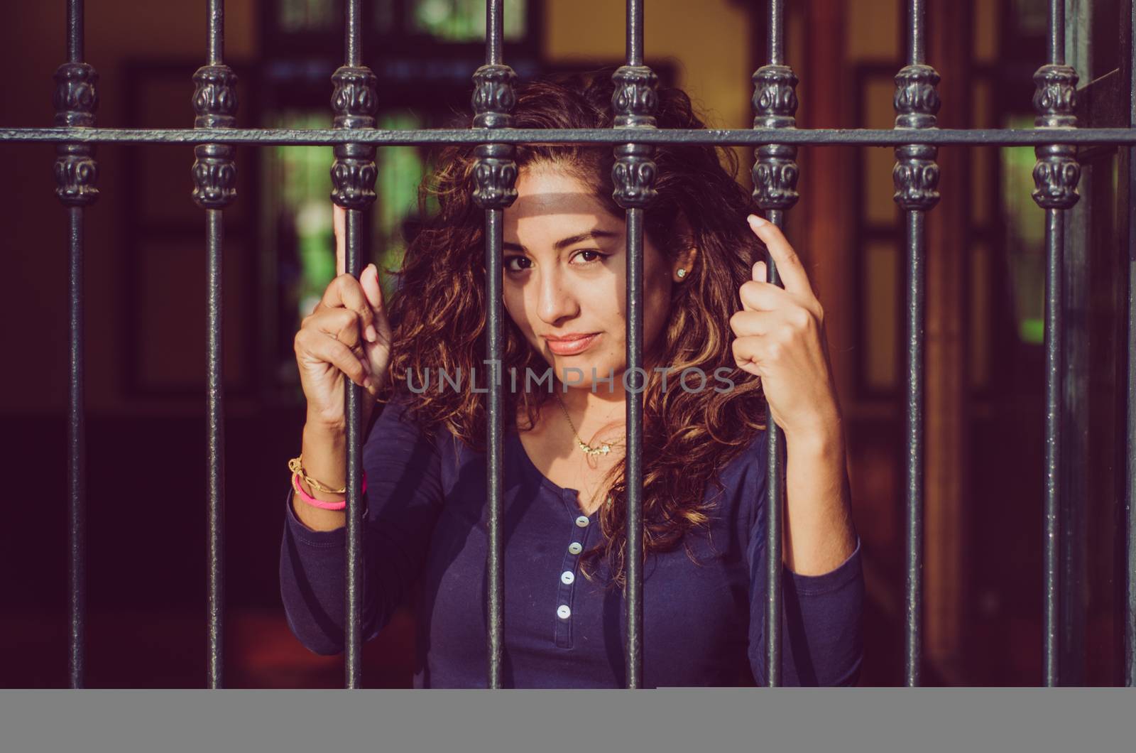 Young girl closed behind bars, network, as in prison. looking sexy with serious and smiling look