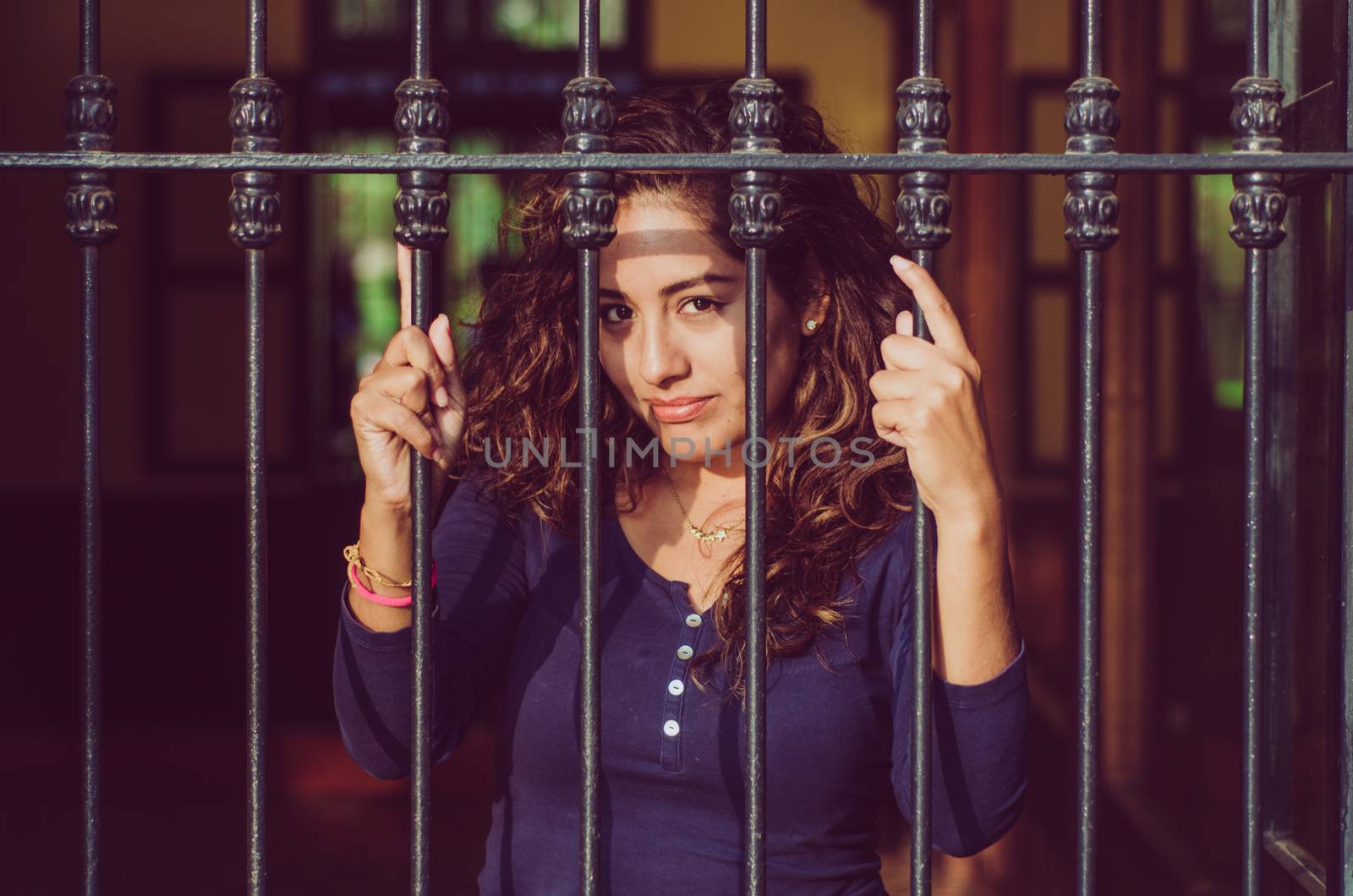 Young girl closed behind bars, network, as in prison. looking sexy with serious and smiling look