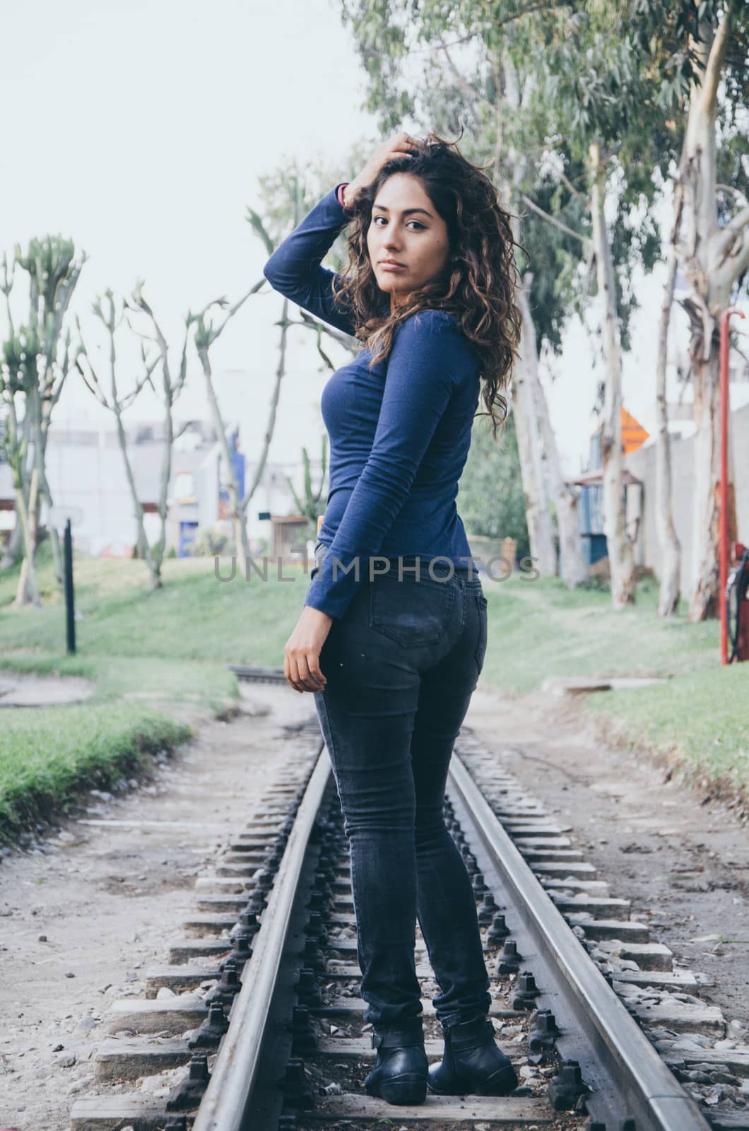 Young sexy girl with long hair in jeans on a railway. Alluring woman looking at camera and smiling