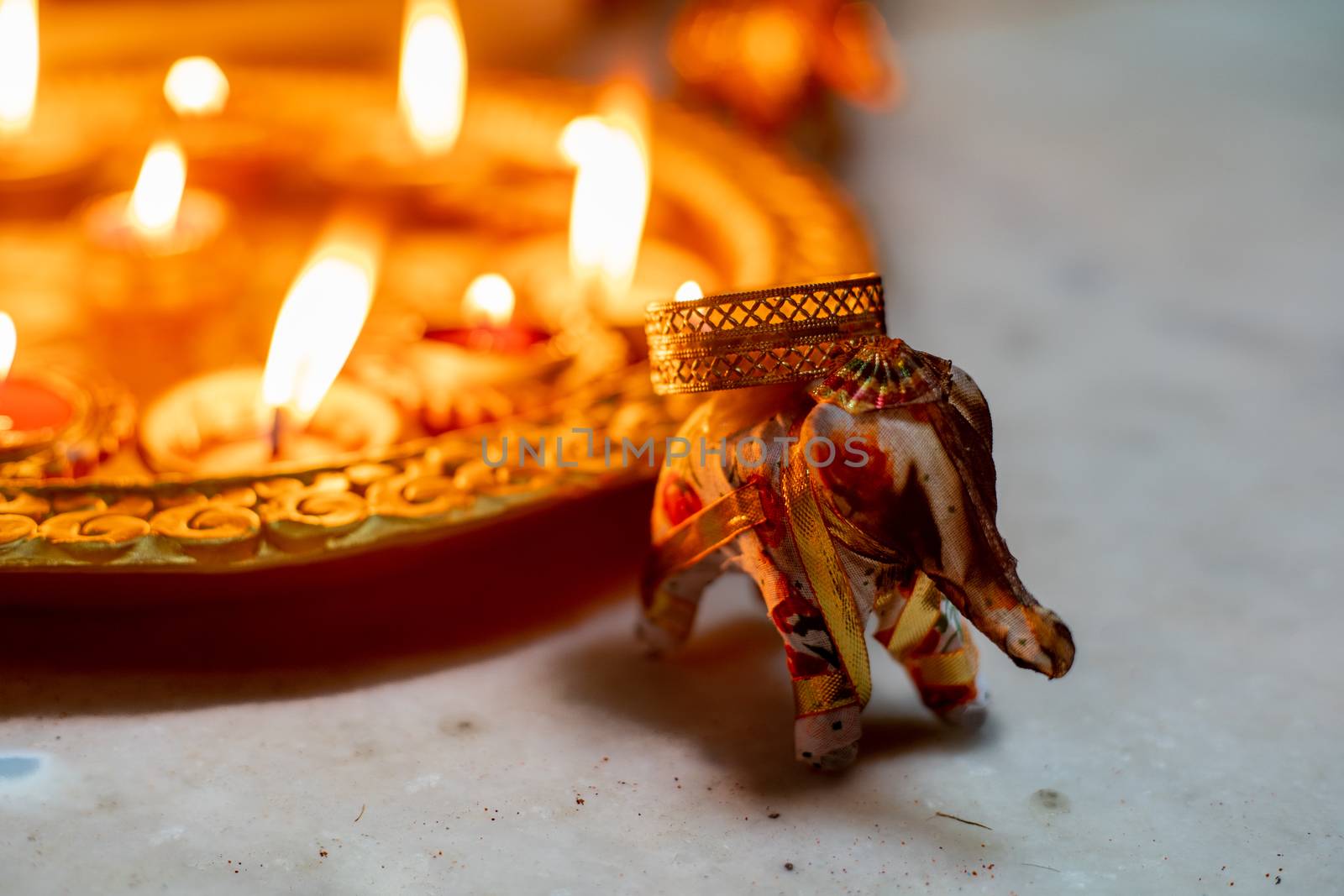 elephant incense holder with smoke coming out of it and beautiful gold painted earthenware diya lamps filled with oil and lit with a flame in the background as decor for the hindu festival of diwali. Shows the beautiful decorations on the hindu festival of diwali where small earthen lamps filled with oil are lit to show the victory of good over evil