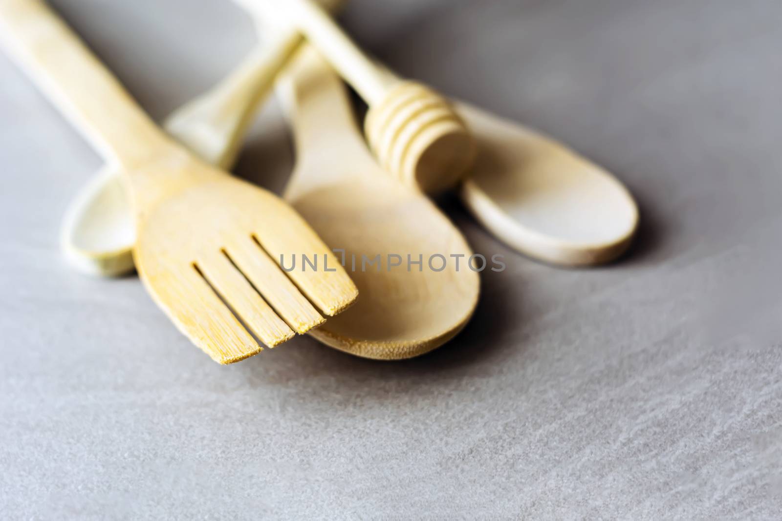 Group of wooden kitchen utensils arranged on a gray marble table. Selective focus on the carving fork.