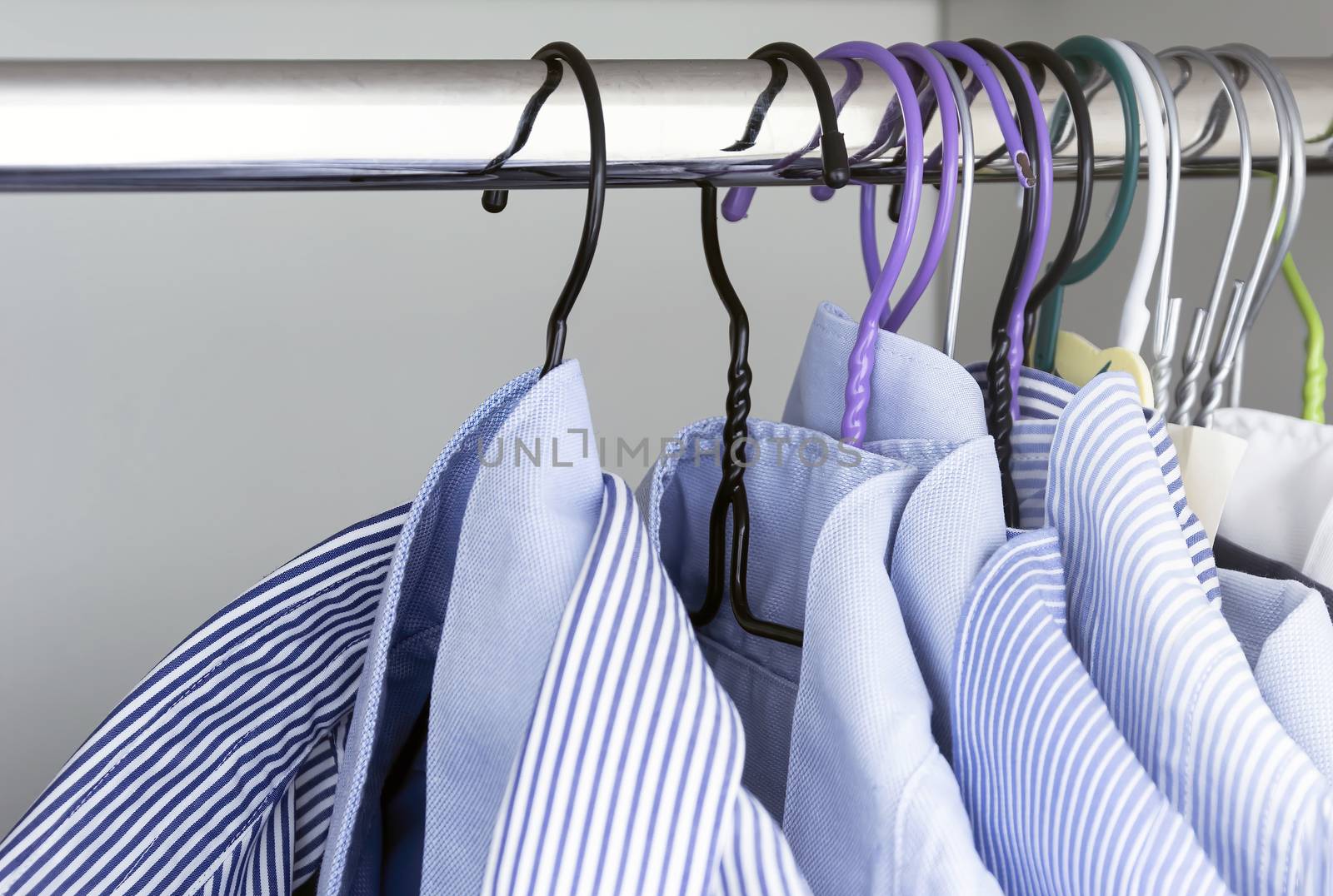 Group of light blue striped shirts hanging on the rod of a white wardrobe. by rarrarorro