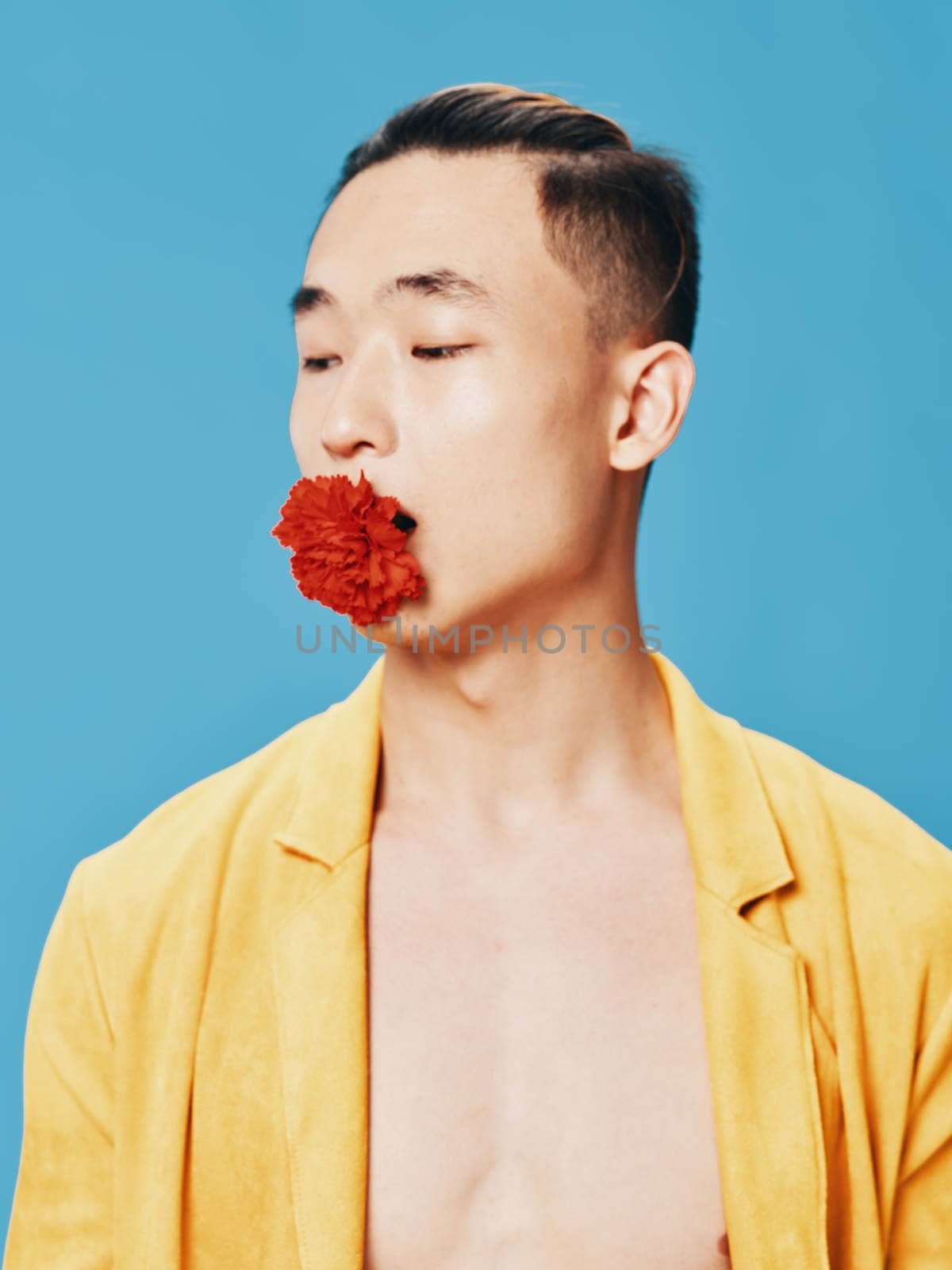 man in an unbuttoned yellow coat on a blue background with a flower in his mouth. High quality photo