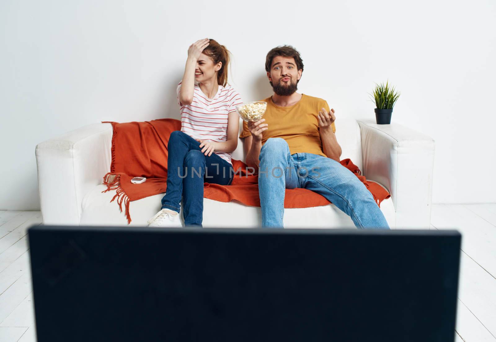 interested man and woman with popcorn on sofa orange plaid and flower in a pot by SHOTPRIME