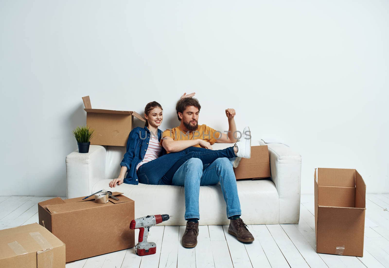 A man and a woman are sitting on the couch near the boxes with things moving the interior of the room by SHOTPRIME