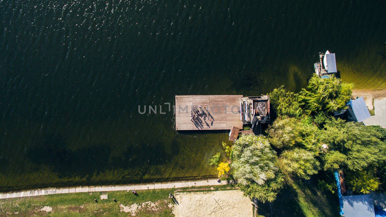 people stand at pier of yacht club against the backdrop of the lake and the shore with green trees. View from above, aerial shooting from drone