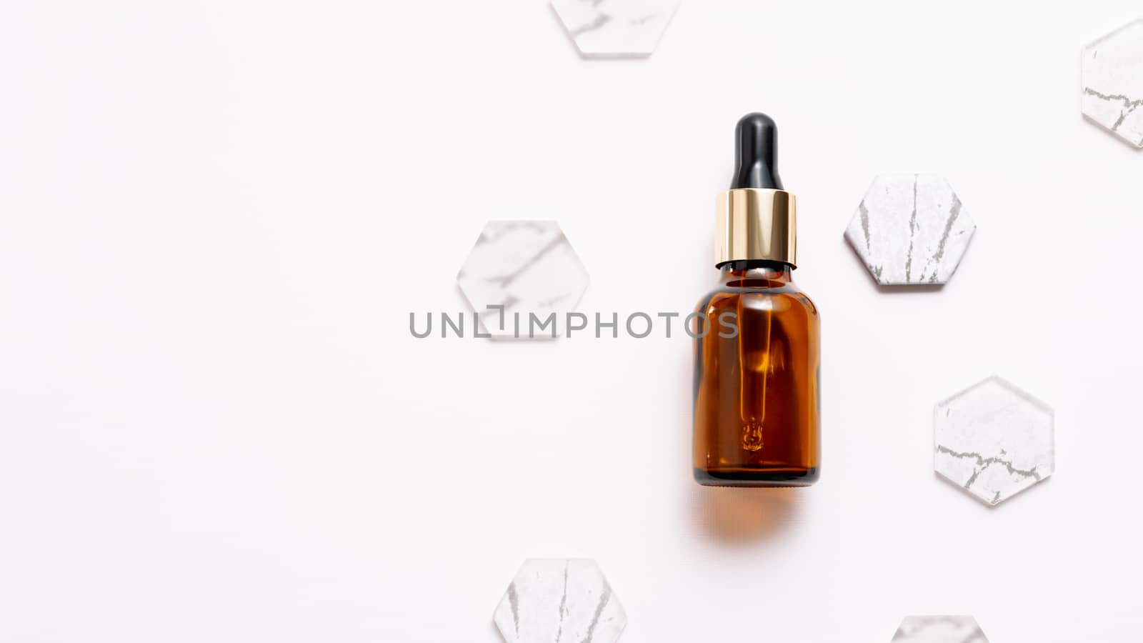 Top view on glass bottles of essential oil or cosmetic serum on white background. White copy space with decorative marble and glass hexagons.