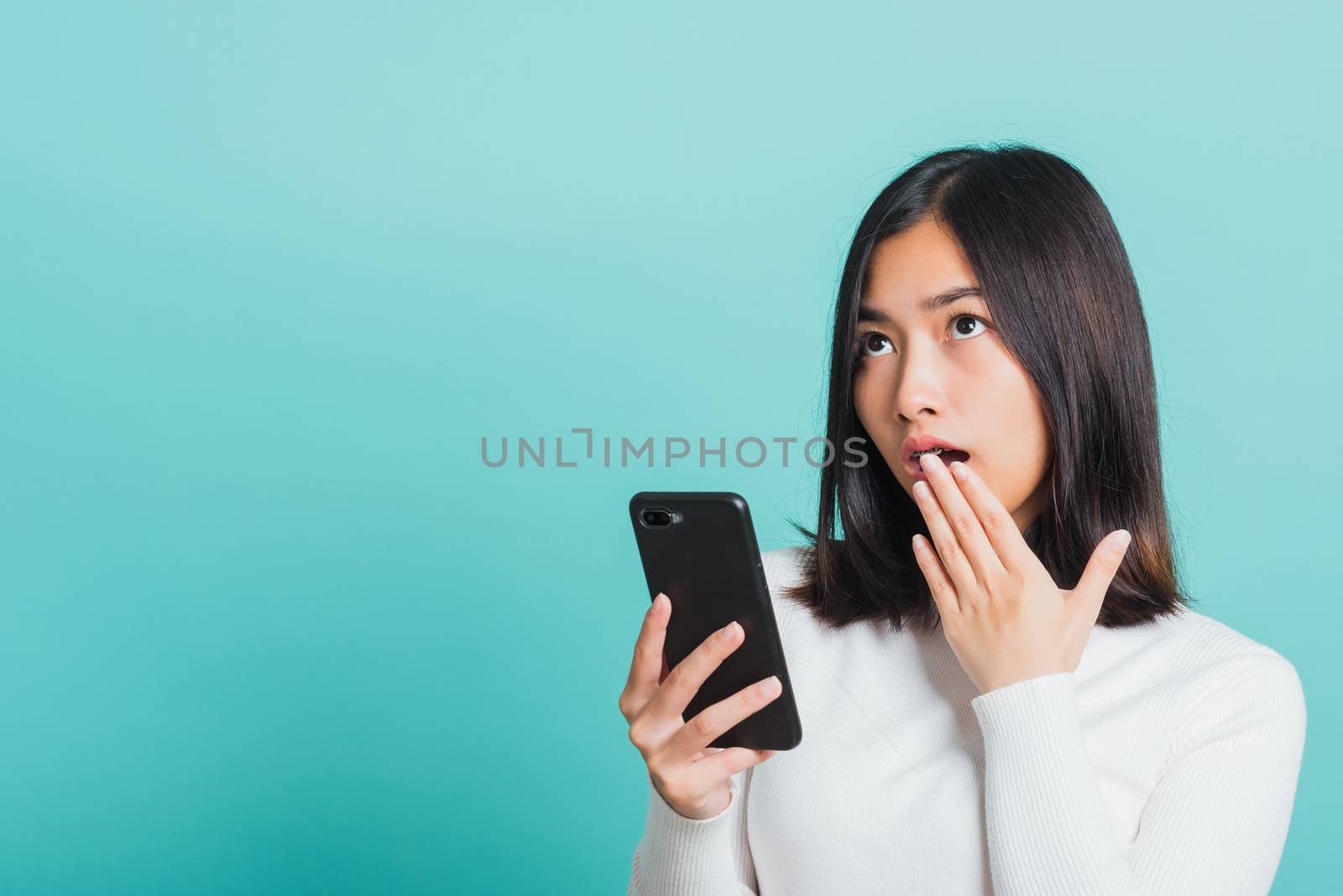 Portrait female anxious scared on the phone seeing bad news, Young beautiful Asian woman surprised shocked with mobile phone close mouth with palm, studio shot isolated on a blue background