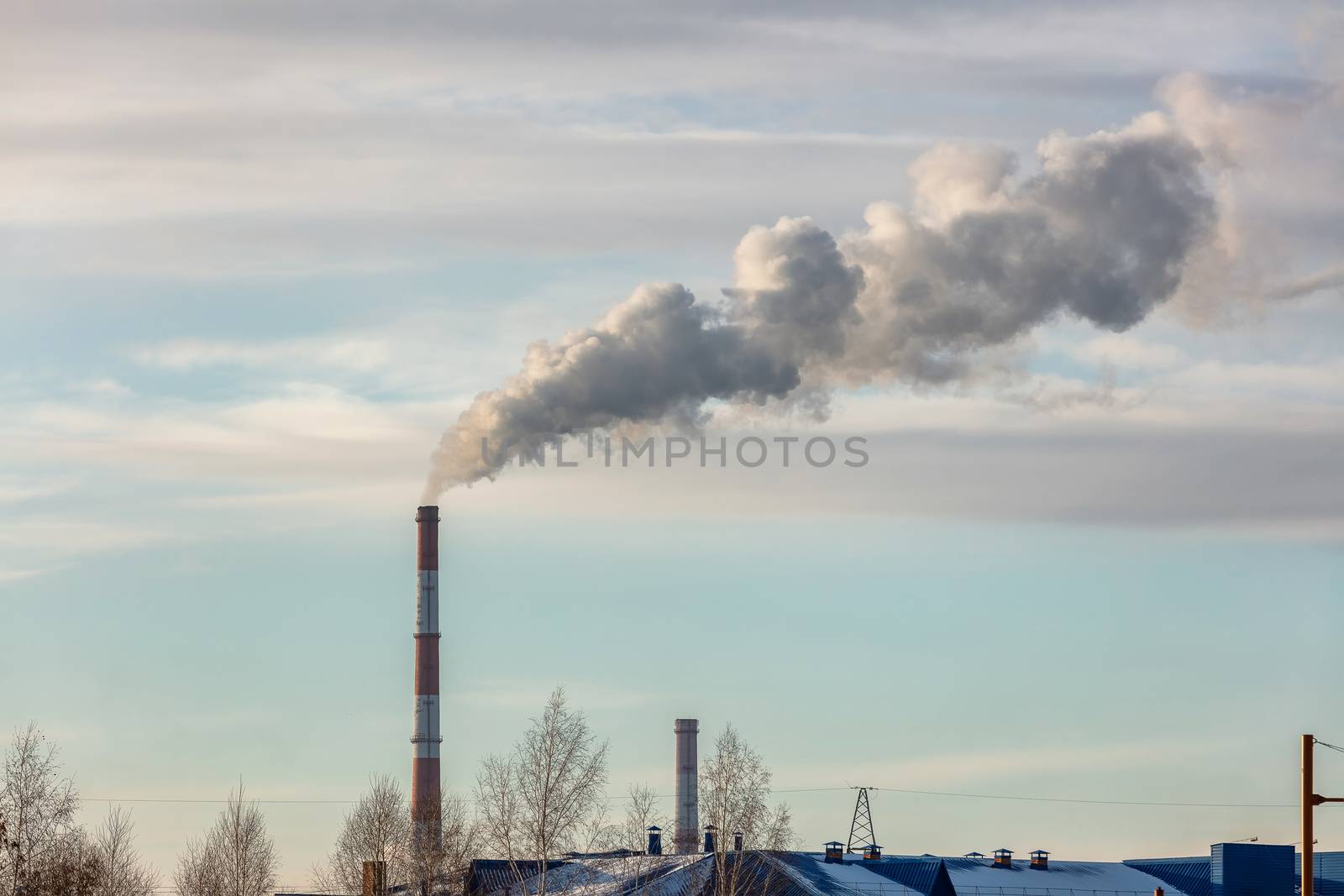 Shot of roof tops and pipes of heating plant that supply central heating system of the city. Smoke coming out of the pipes. Blue cloudy sky as a background. Industrial landscape. Barnaul, Russia by DamantisZ