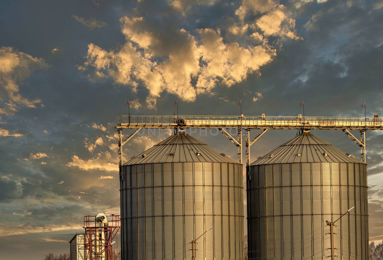 Low angle shot of grain storage units. Beautiful sunset sky background. Golden hour. Altai Krai, Siberia, Russia.