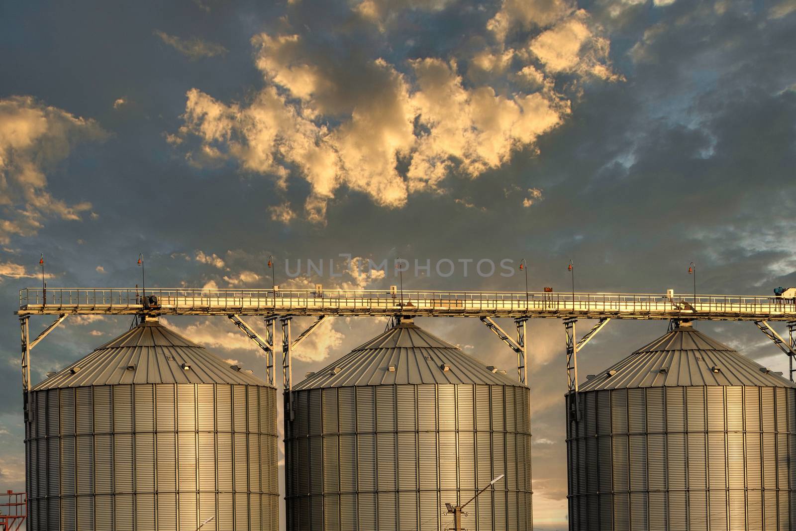 Low angle shot of grain storage units. Beautiful sunset sky background. Golden hour. Altai Krai, Siberia, Russia.