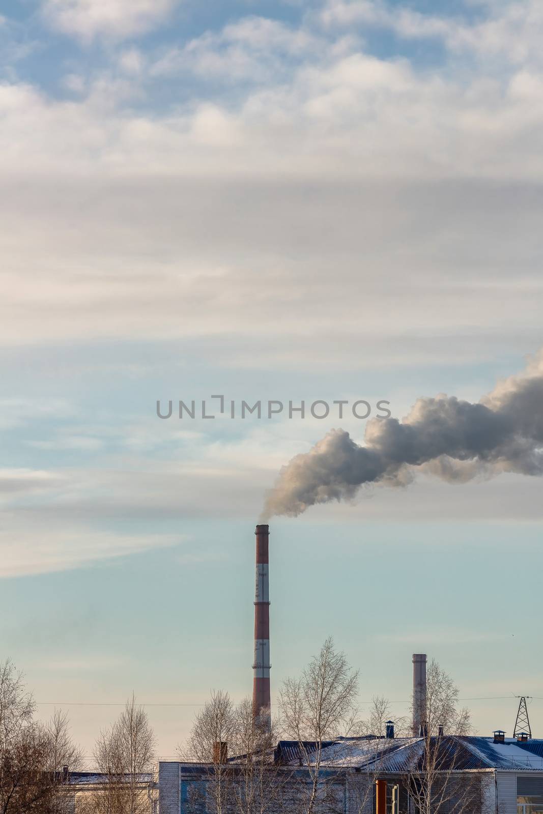 Shot of roof tops and pipes of heating plant that supply central heating system of the city. Smoke coming out of the pipes. Blue cloudy sky as a background. Industrial landscape. Barnaul, Russia.