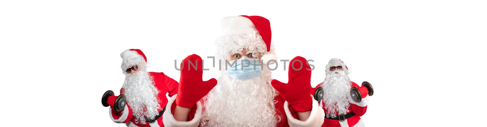 Santa Claus wearing a medical mask, having his both hands up, eyes wide open in warning gesture. Two Santa Clauses working out in the background behind him. Isolated on white background. Banner size, copy space by DamantisZ