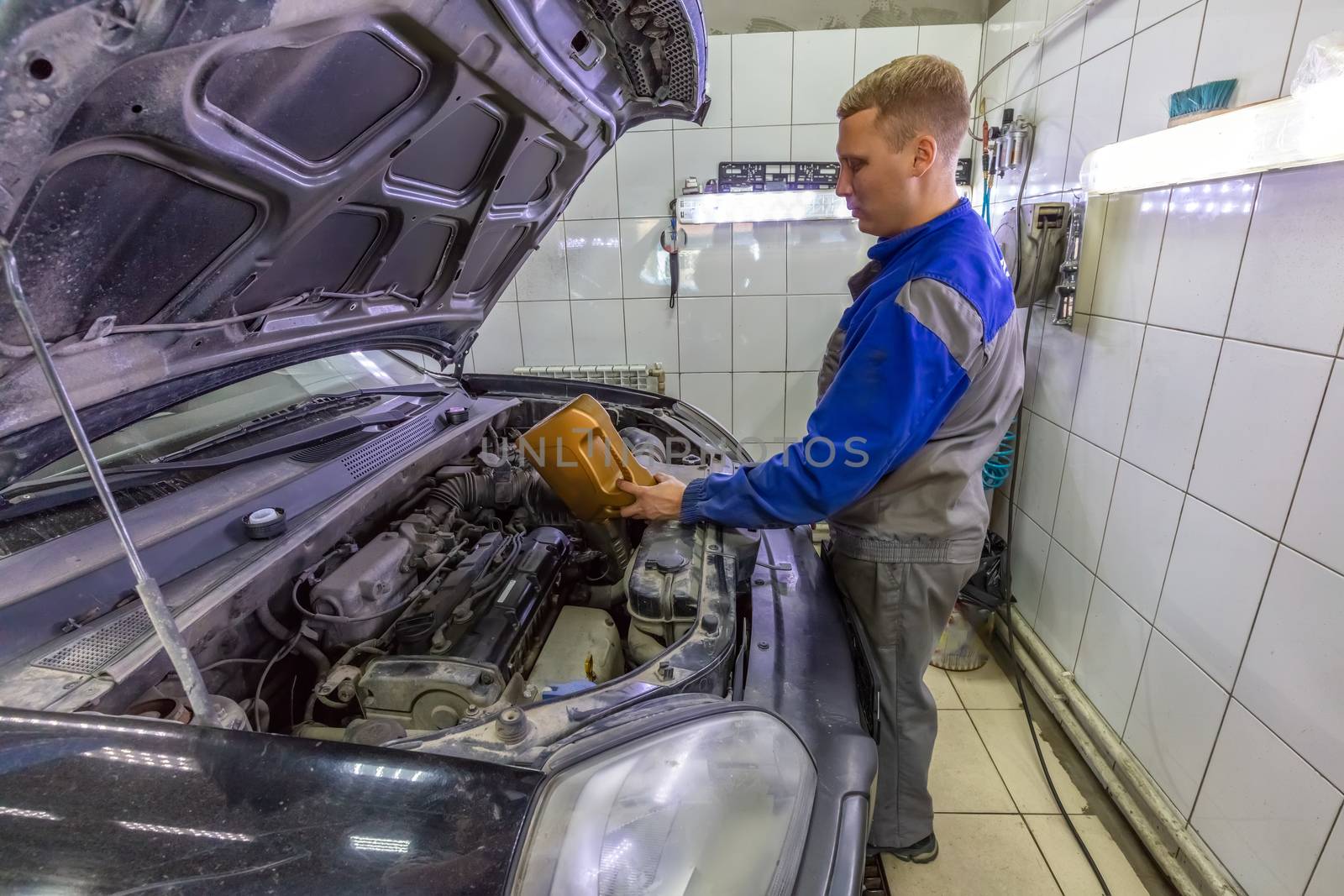 Car mechanic replacing and pouring oil into engine at car service station during regular check-up routine.