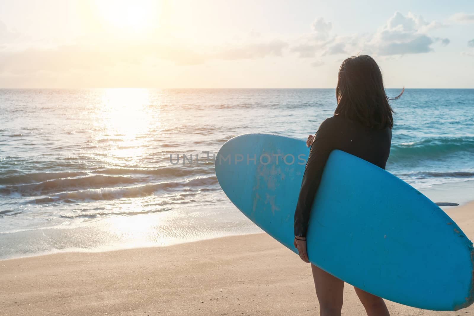 Surfer woman carrying their surfboards on sunset beach with sun light  background