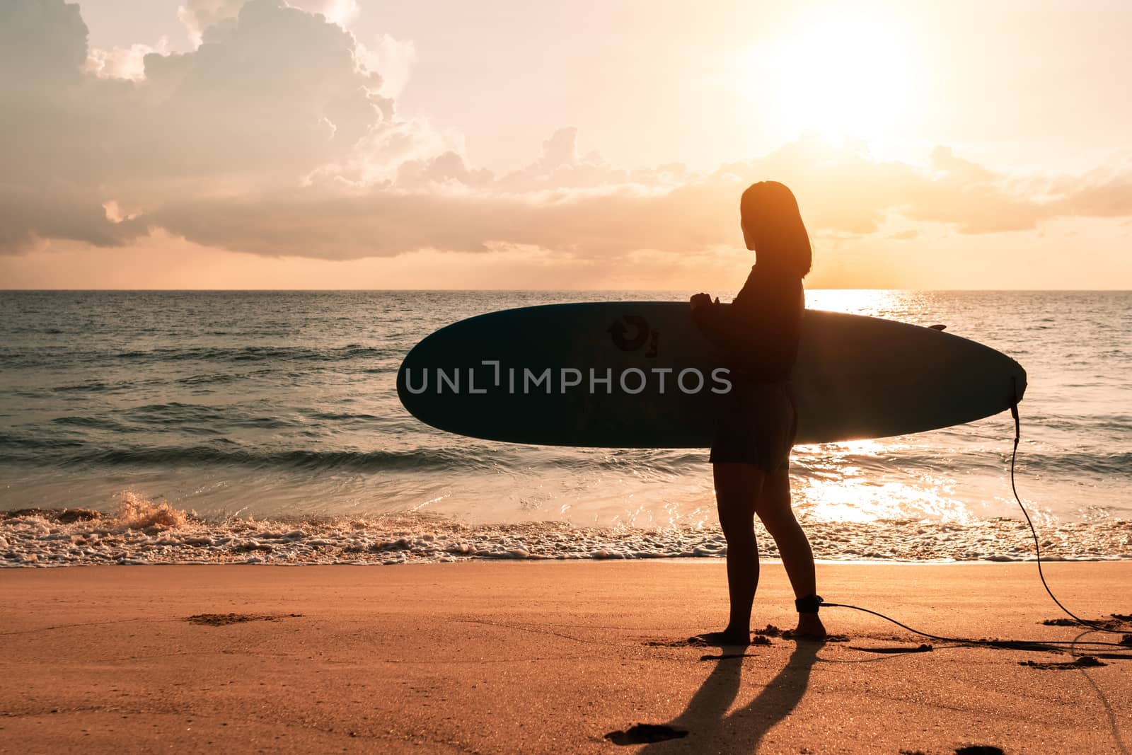 Silhouette of surfer woman carrying their surfboards on sunset beach with sun light  background