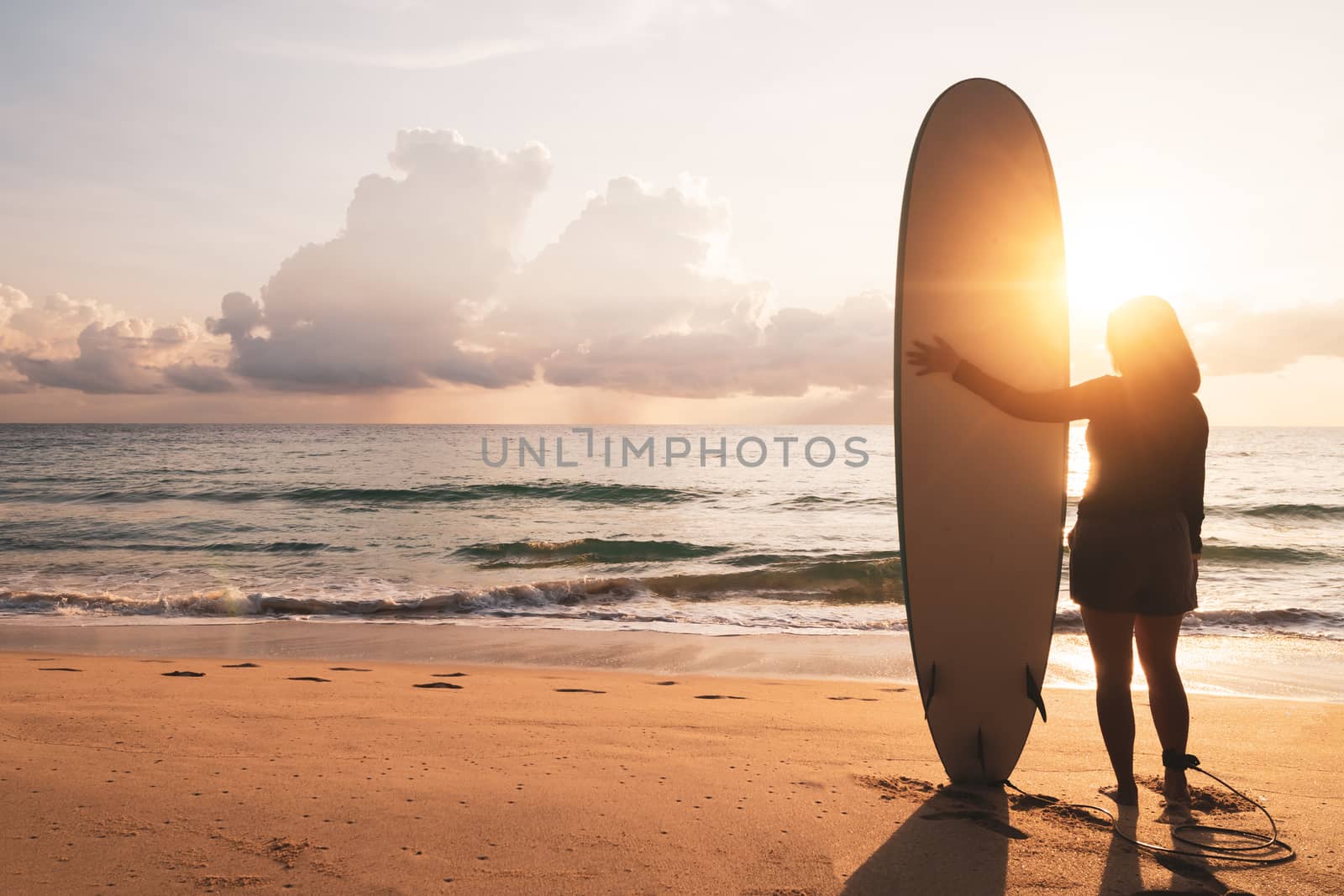 Silhouette of surfer woman carrying their surfboards on sunset beach with sun light  background