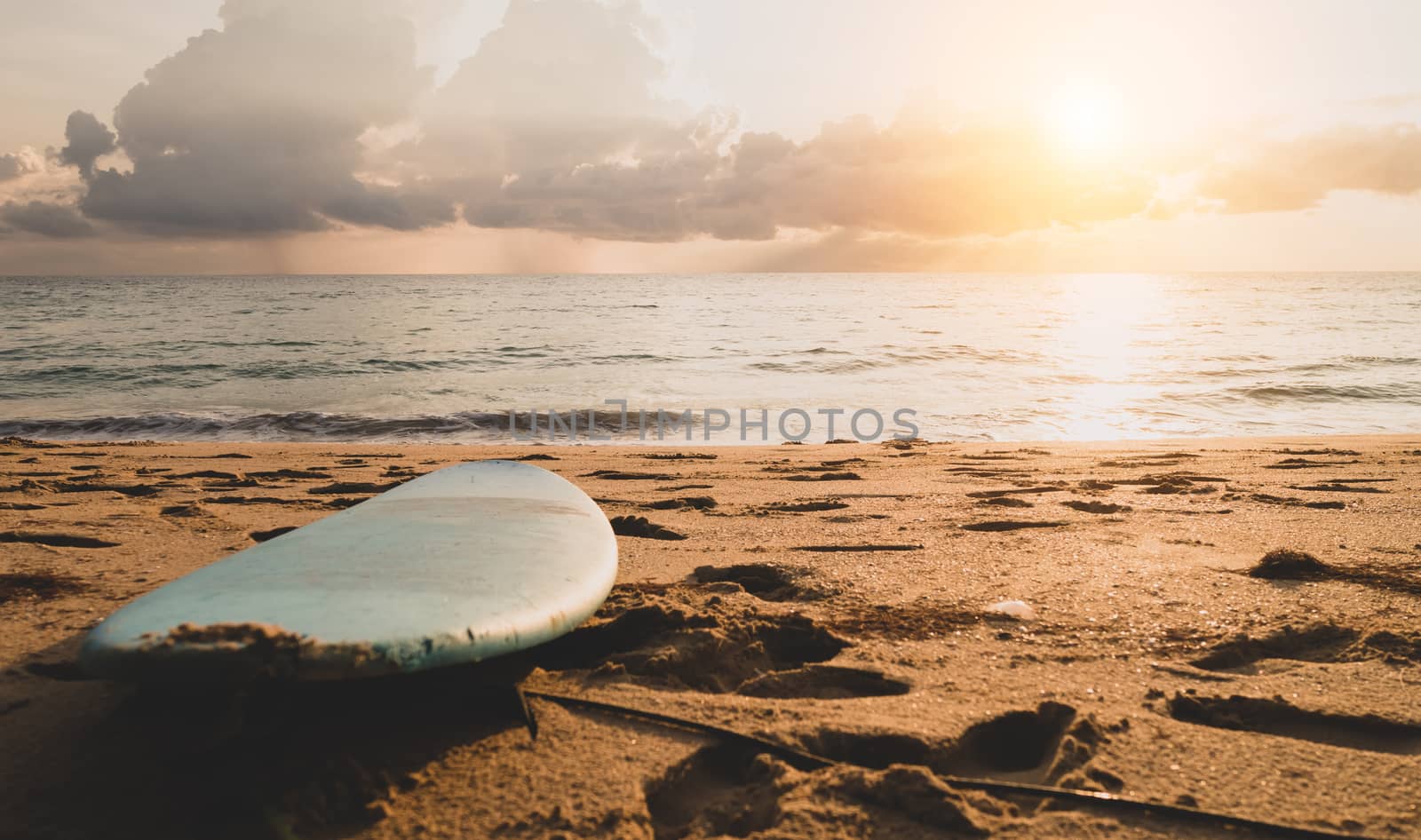 Surfboard on sand at summer beach with sunset light background.