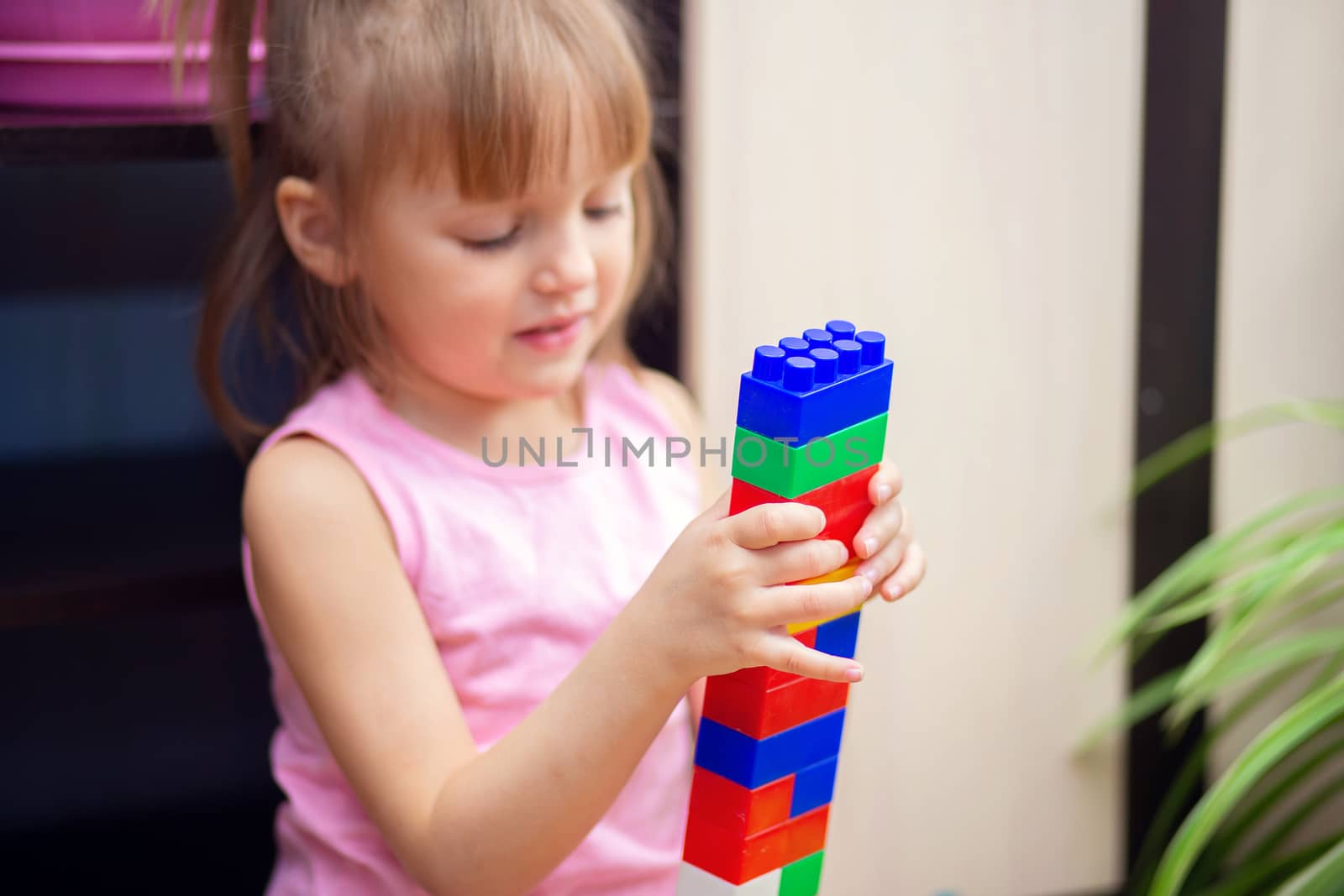 A little girl at home plays with a plastic colored constructor. A child built a tower from parts of a children's designer