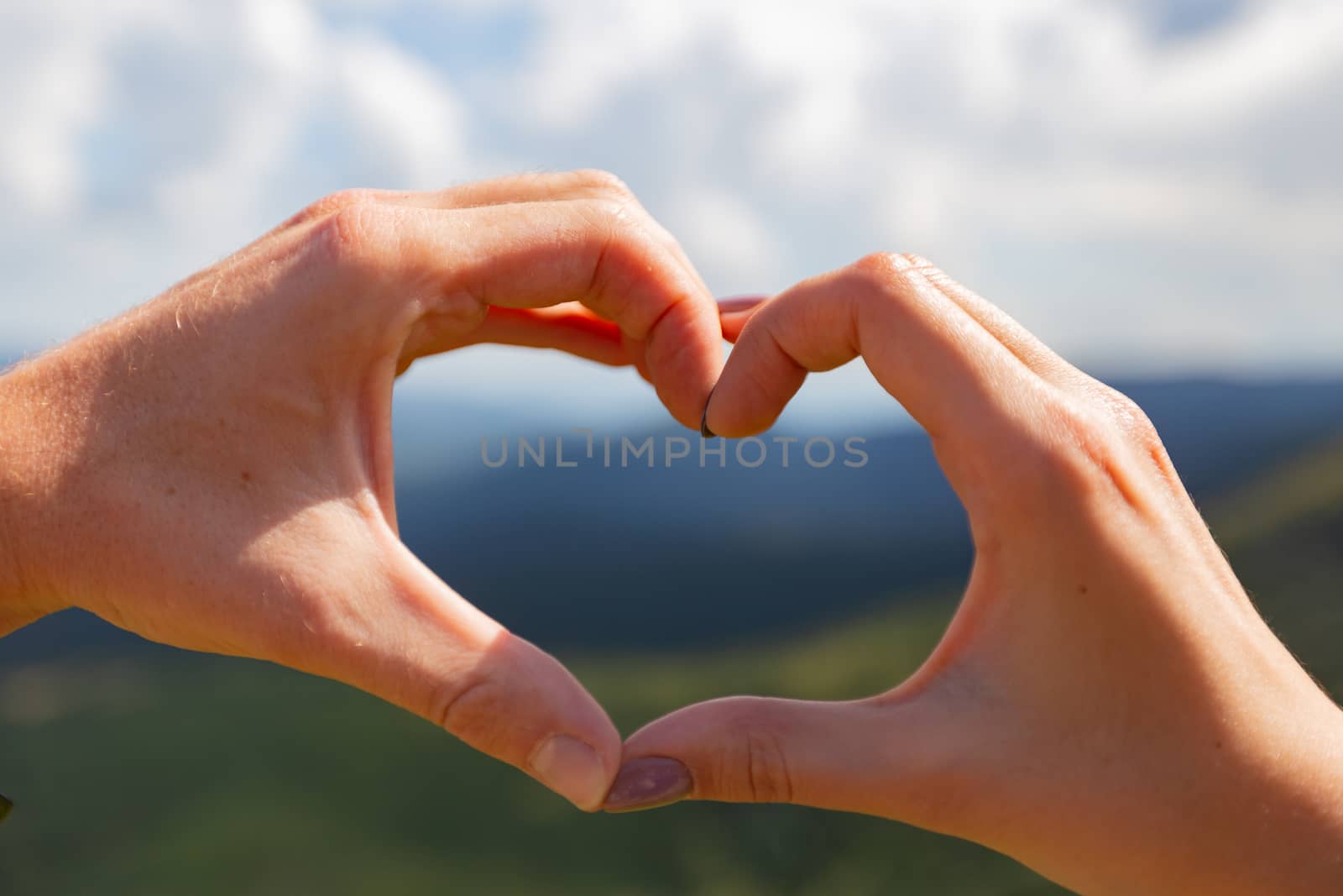 Male and female hand folded heart against the sky. Traveling in the Carpathians.