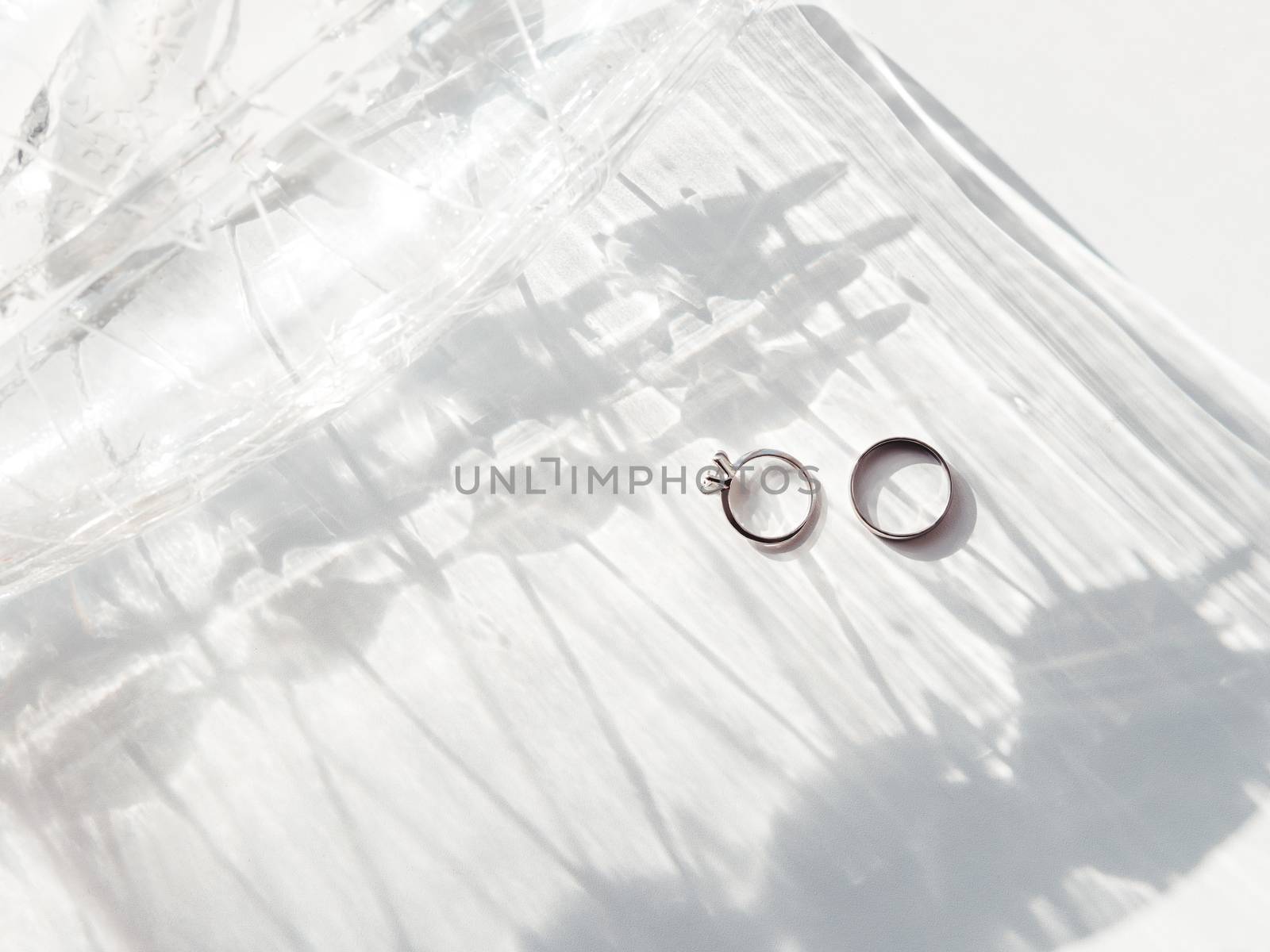 Top view on wedding and engagement rings with diamond. Symbol of love and marriage on white background with laced shadow. Sunlight on white background.