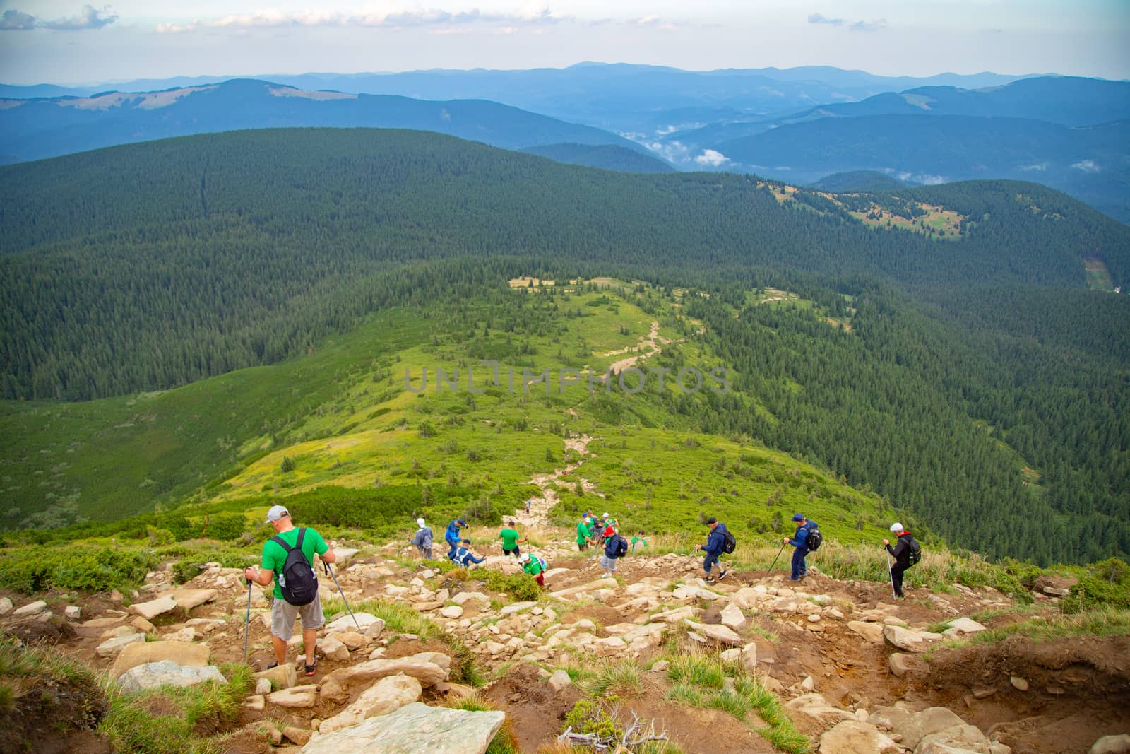 People descend down a large green mountain range. Mountain Hiking by TrEKone