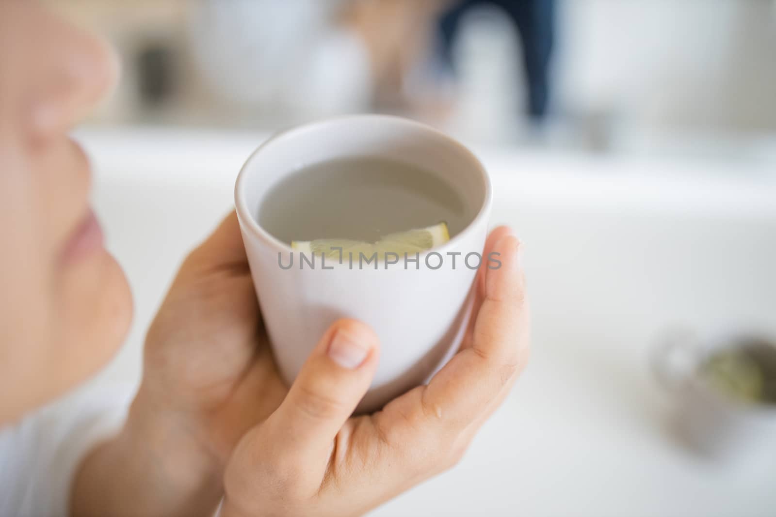 Woman gently blowing on hot cup of lemon tea with a lemon slice floating inside. Woman smelling lemon-flavored drink in cup. Sweet citric beverages