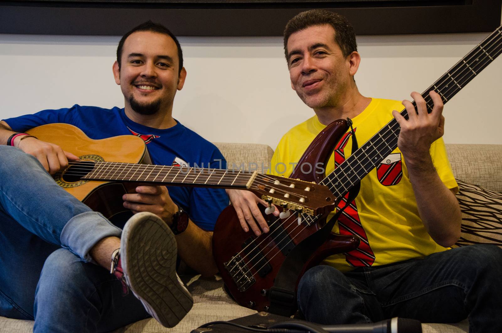 Young smiling people playing guitars sitting on a sofa at home