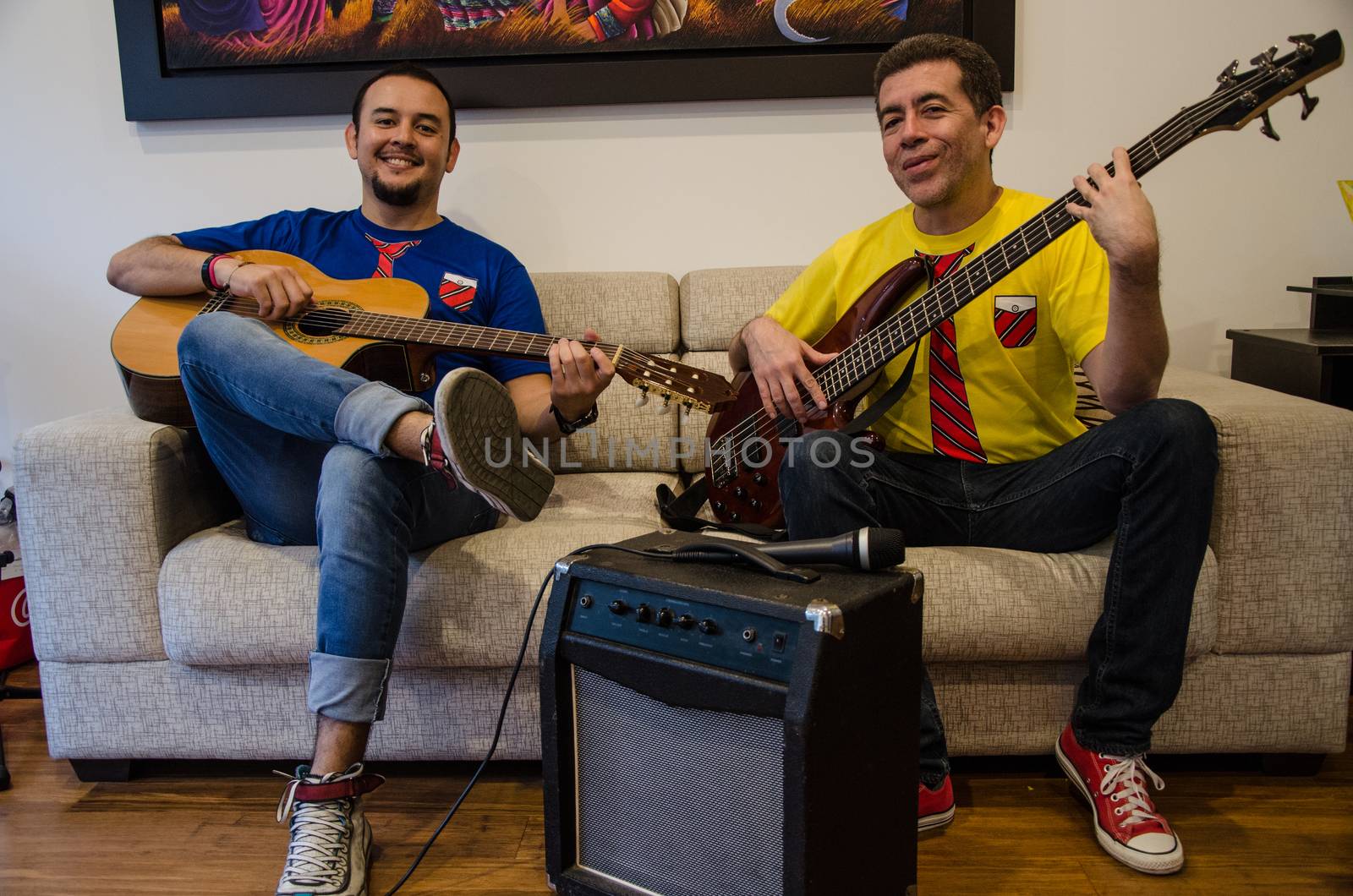 Young smiling people playing guitars sitting on a sofa at home with an amplifier