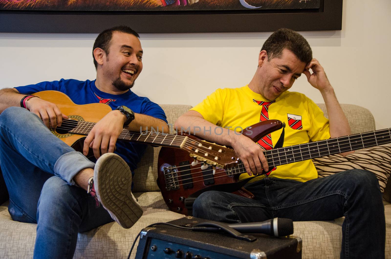 Young smiling people playing guitars sitting on a sofa at home