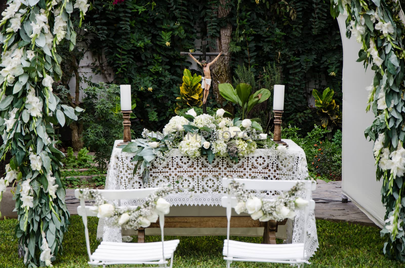 White pillars with bouquets of roses surround place prepared for wedding ceremony