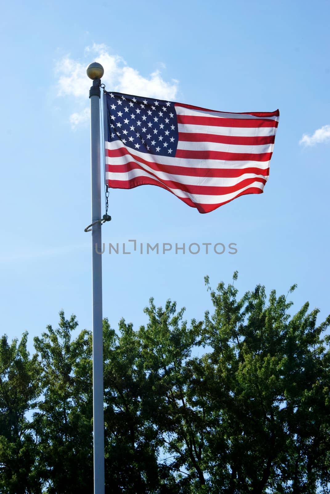 A vertical composition of an American flag flapping in the wind during the sunny daylight hours.