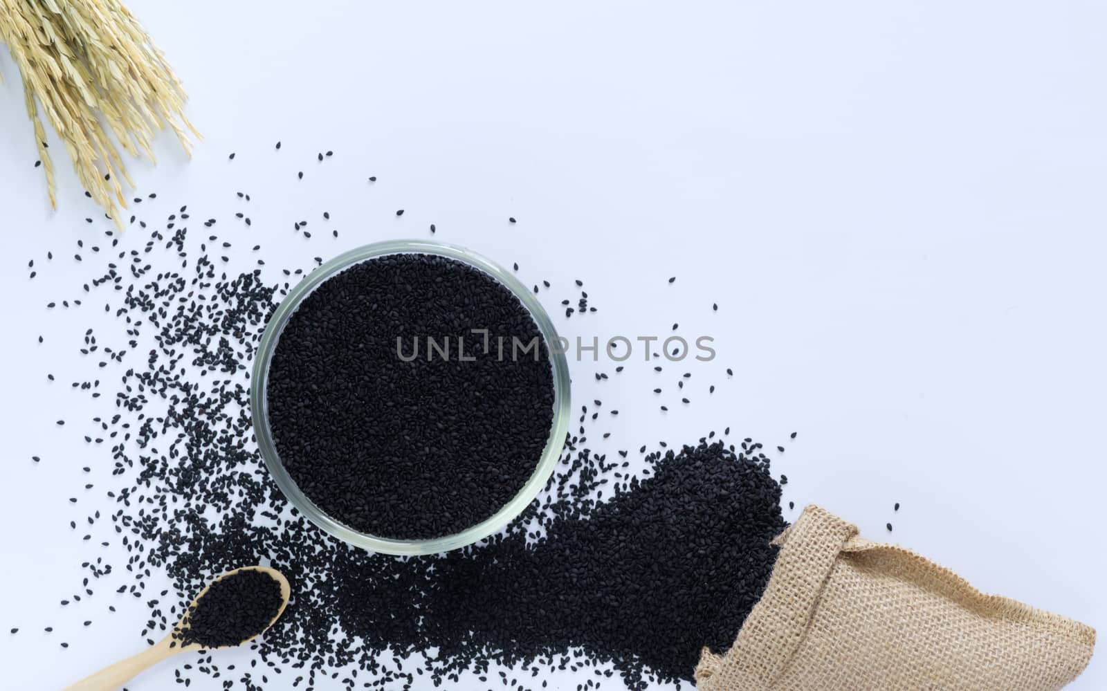 Black sesame in a cup on a white background with wooden spoon, sacks and ears of rice are elements.