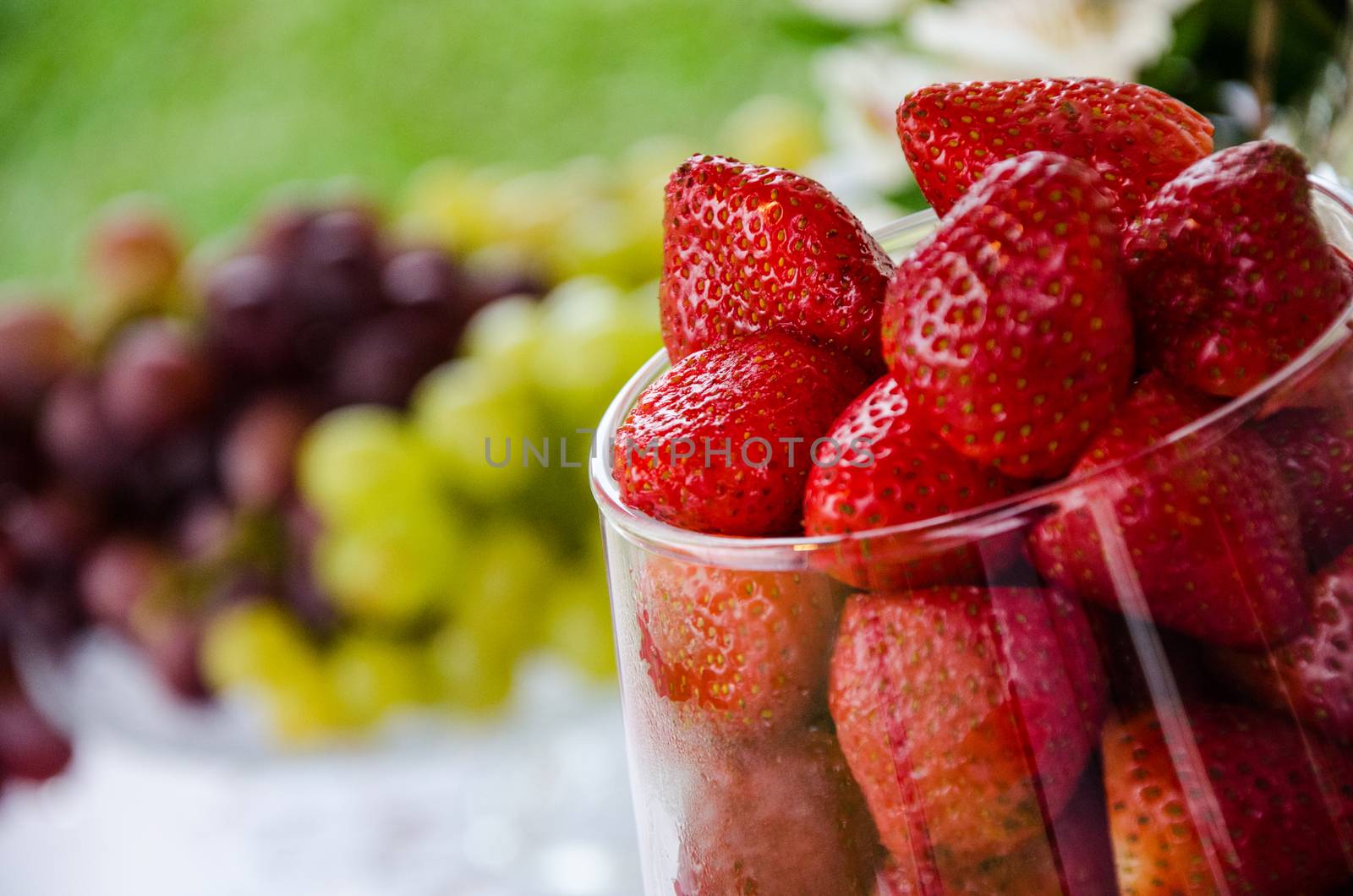 Glass bowl with fresh strawberries with blurred grapes background