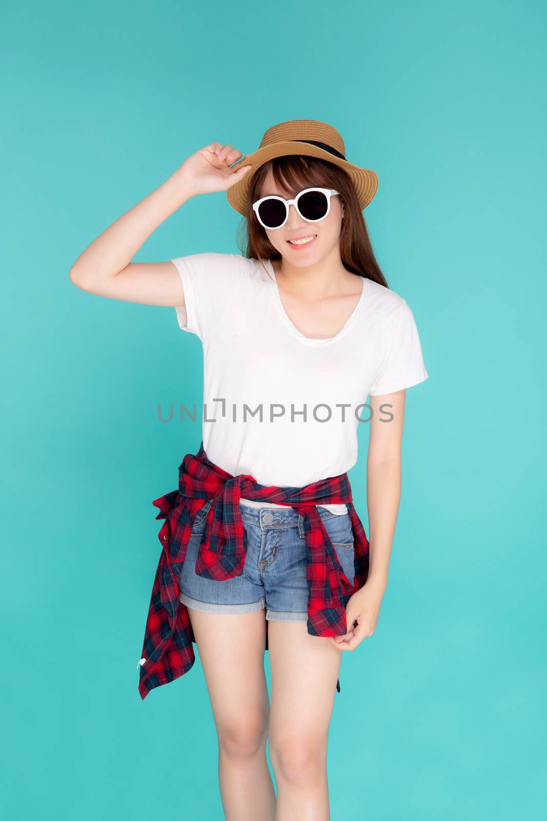 Beautiful portrait young asian woman wear sunglasses holding hat smile cheerful and enjoy travel summer trip holiday in vacation isolated blue background, tourist happy asia girl confident and excited.
