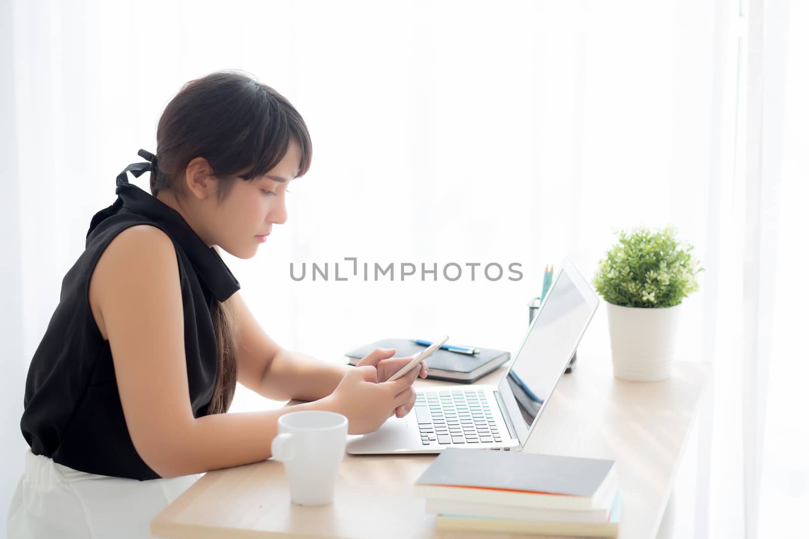 Beautiful young asian woman working laptop computer online to internet and texting message on smart mobile phone, freelance using notebook, business and communication concept.