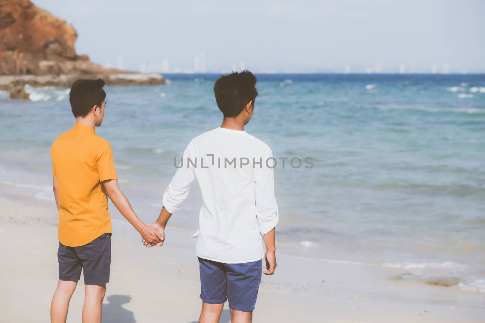 Back view homosexual young asian couple standing together on beach in summer, asia gay holding hands going sea for leisure and relax with romantic and happy in vacation at sea, LGBT with legal concept.