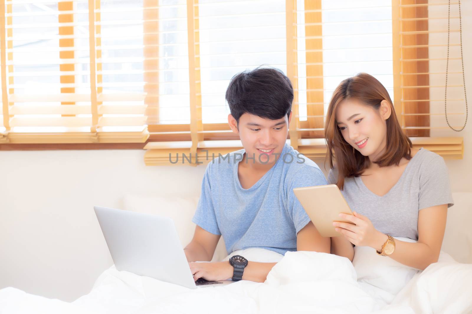 Beautiful young asian couple cheerful freelance working with man using laptop and woman using tablet on couch, family relax and sharing communication together at home, lifestyle concept.