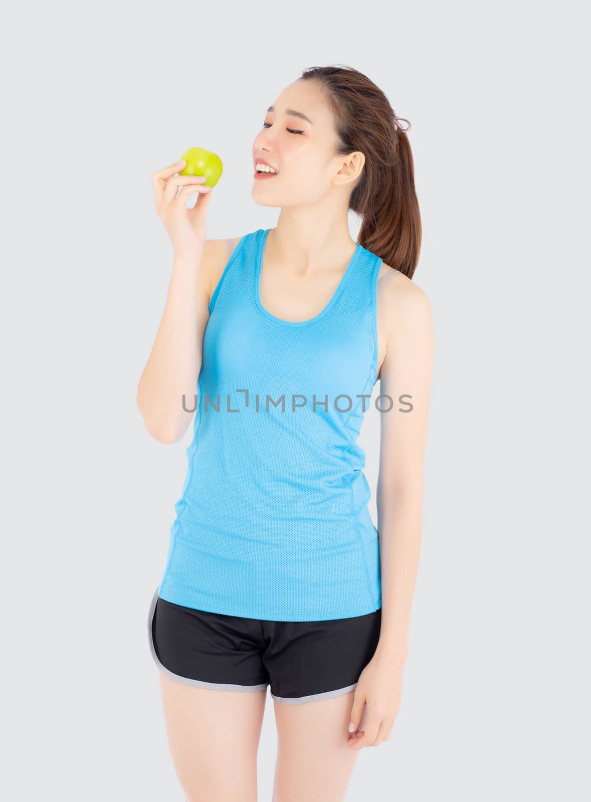Beautiful portrait young asian woman in sport with satisfied and holding and eat green apple isolated on white background, girl asia have shape and wellness, exercise for fit with health concept.