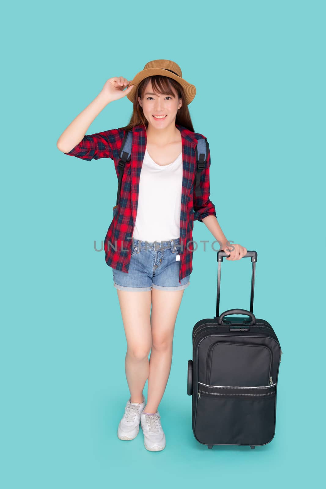 Beautiful young asian woman pulling suitcase isolated on blue background, asia girl having expression is cheerful holding luggage walking in vacation with excited, journey and travel concept.