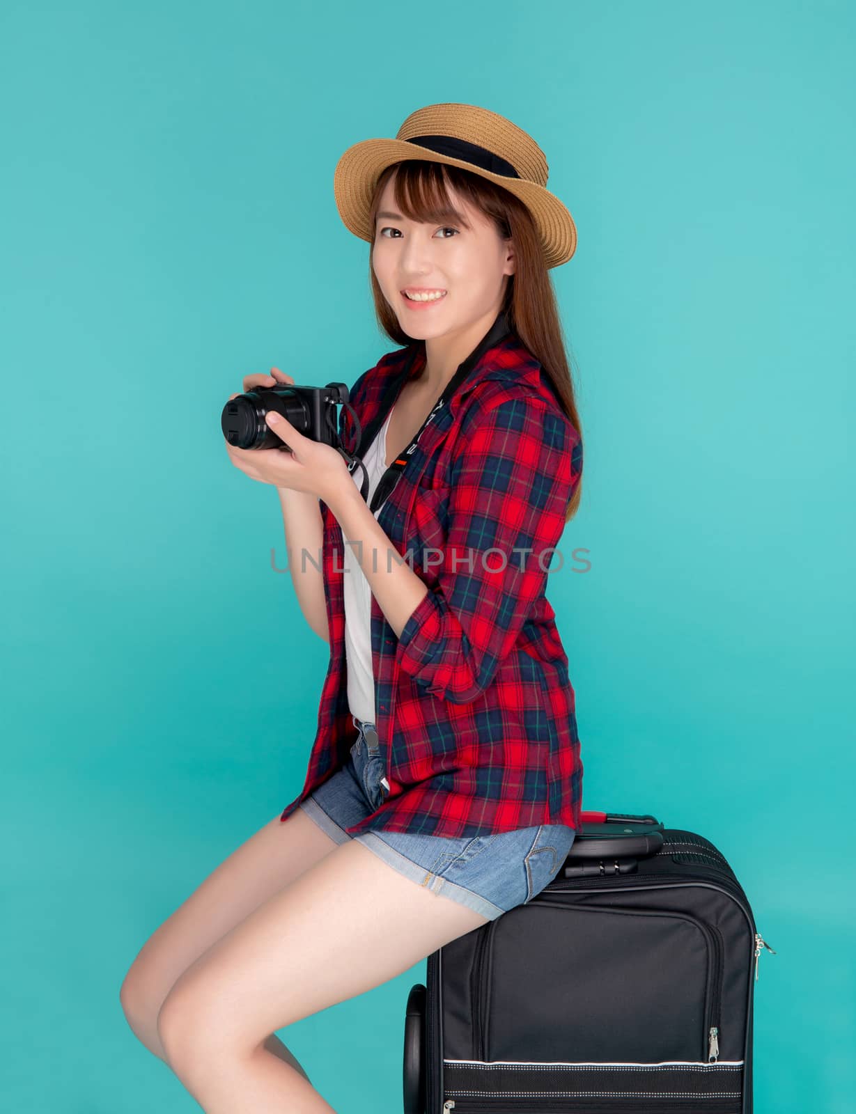 Beautiful portrait young asian woman sitting on luggage smiling and travel summer trip for abroad in vacation, happy asia girl holding camera sitting on suitcase for journey with cheerful in holiday.