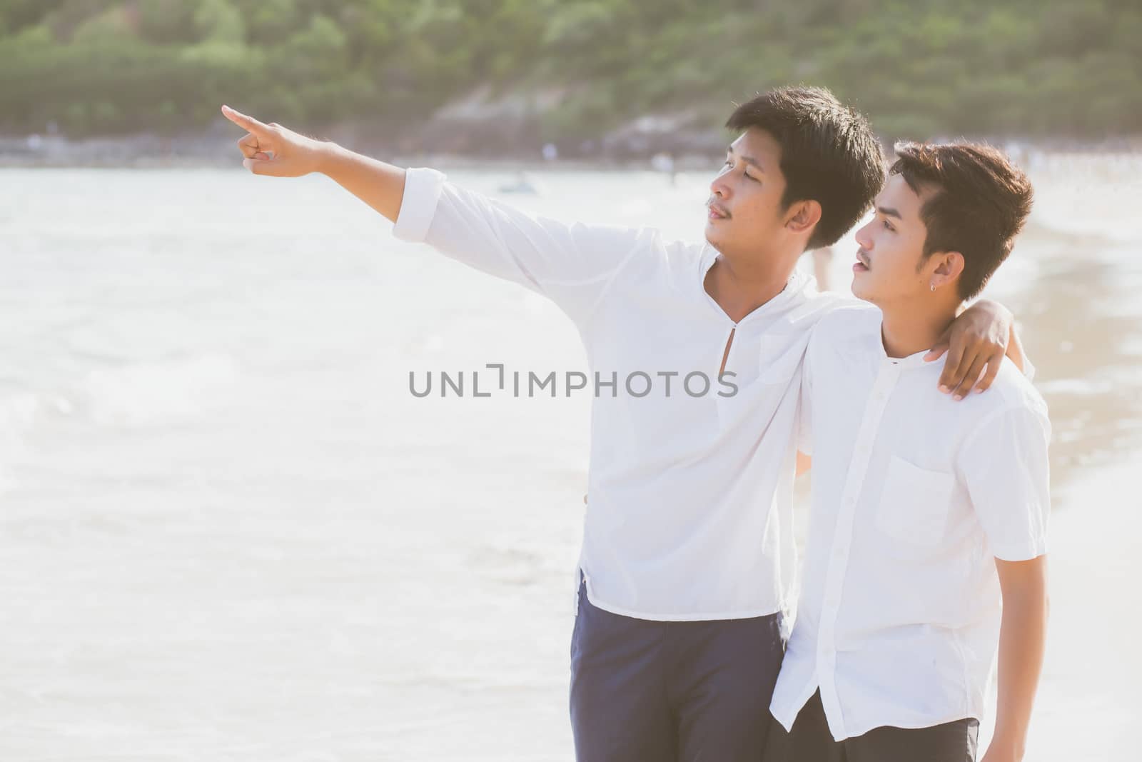 Homosexual portrait young asian couple standing pointing something together on beach in summer, asia gay going sea for leisure with romantic and happy in vacation at sea, LGBT with legal concept.